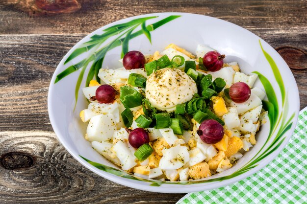 Salade d'oeufs et d'oignons, groseilles décorées, dans une assiette blanche sur une table en bois.