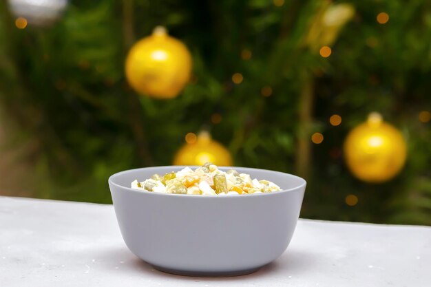 Photo salade olivier avec du poulet, des légumes, des cornichons contre l'arbre de noël, un apéritif slavon traditionnel ukrainien pour célébrer la veille du nouvel an.