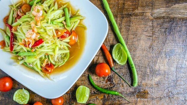 Salade de papaye de la cuisine thaïlandaise sur une assiette avec du citron et de la tomate sur une vue de dessus de fond en bois