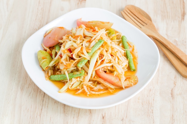 Salade de papaye dans une assiette blanche sur une table en bois, nourriture thai locale