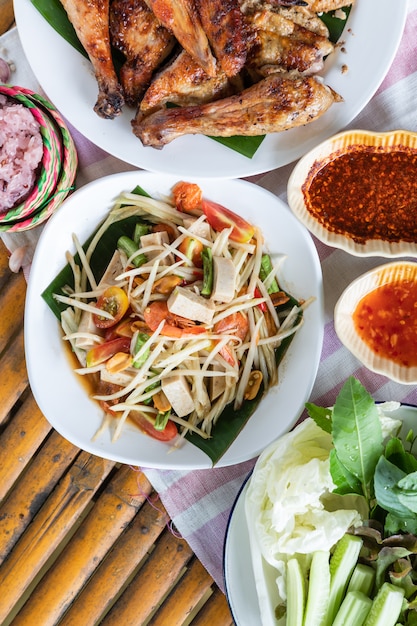 Photo salade de papaye et poulet grillé en plaque blanche sur fond de bambou