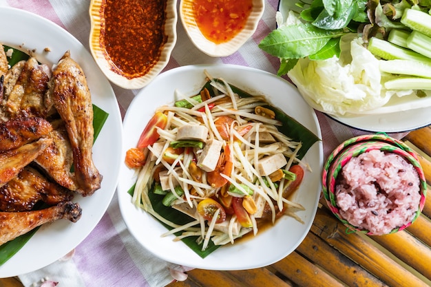 Salade de papaye et poulet grillé en plaque blanche sur fond de bambou