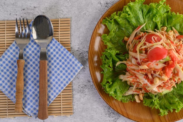 Photo salade de papaye thaïlandaise dans une assiette en bois avec cuillère et fourchette