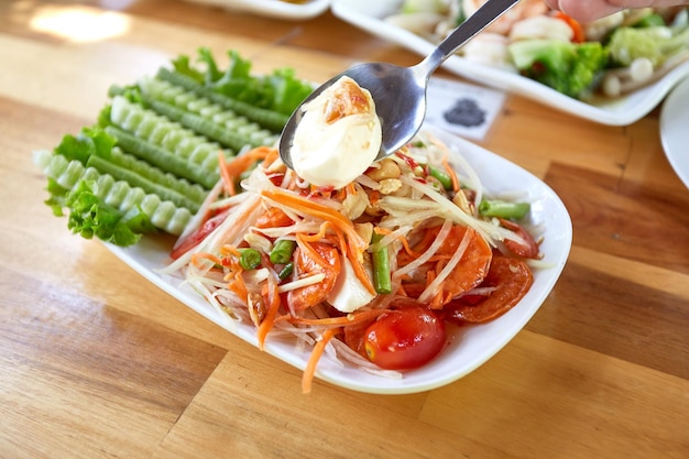 Salade de papaye thaïlandaise avec œuf salé sur table à manger en bois Cuisine thaïlandaise