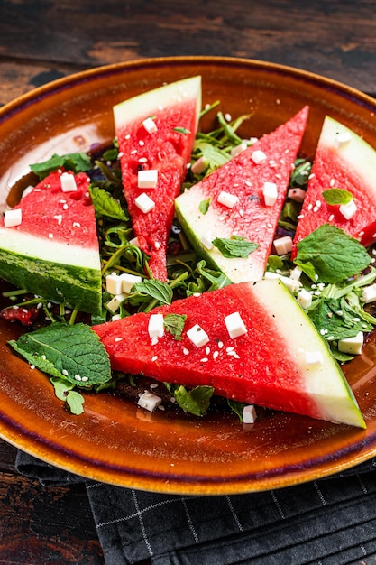 Salade de pastèque fraîche d'été avec fromage feta, roquette, oignons dans une assiette rustique. Fond sombre. Vue de dessus.