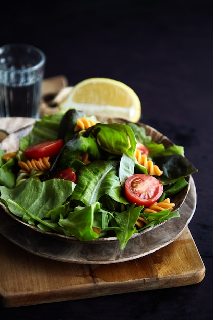 Salade de pâtes Fusilli avec tomates colorées et feuilles de basilic sur bois foncé