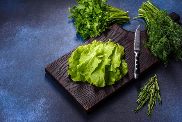 Salade de persil et d'aneth sur une planche à découper sombre sur un fond de béton bleu