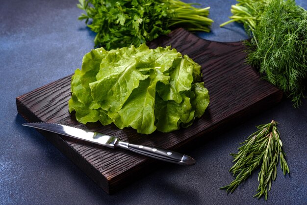 Salade de persil et d'aneth sur une planche à découper sombre sur un fond de béton bleu