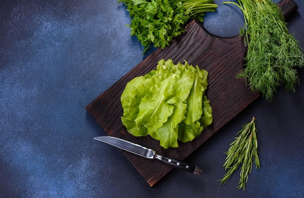 Salade de persil et d'aneth sur une planche à découper sombre sur un fond de béton bleu