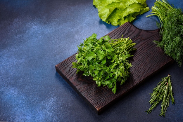 Salade de persil et d'aneth sur une planche à découper sombre sur un fond de béton bleu