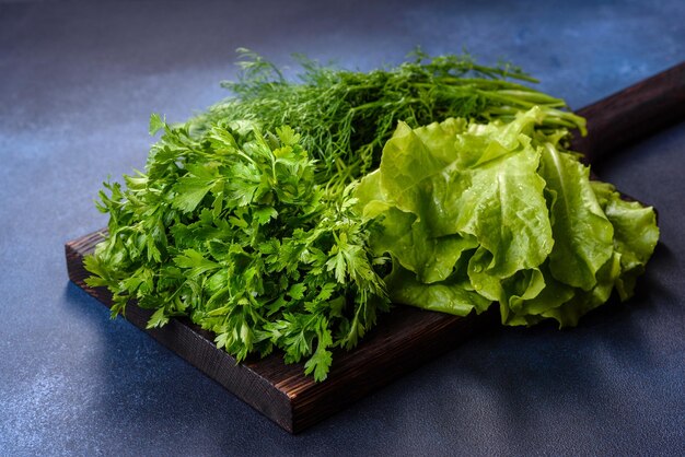 Salade de persil et d'aneth sur une planche à découper sombre sur un fond de béton bleu