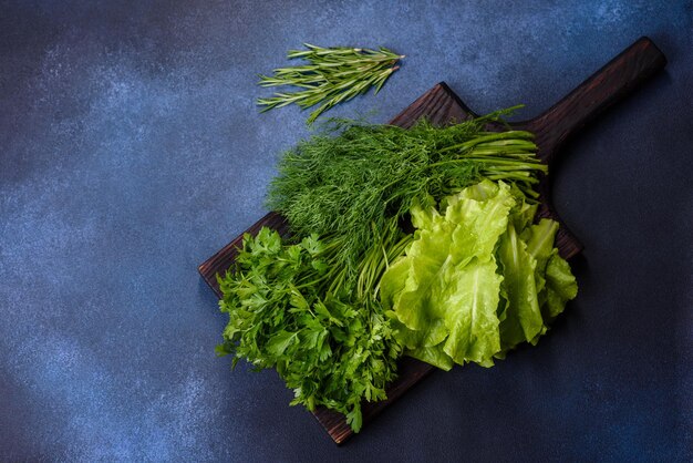 Salade de persil et d'aneth sur une planche à découper sombre sur un fond de béton bleu