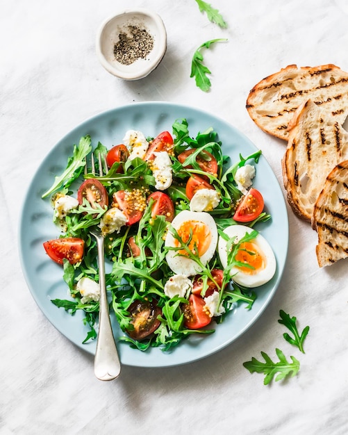 Salade de petit-déjeuner roquette tomates cerises mozzarella et œuf dur avec vinaigrette citron moutarde à l'huile d'olive sur fond clair