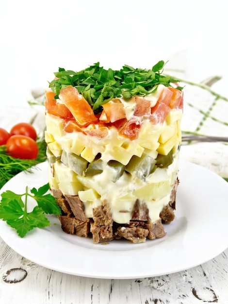 Salade de pommes de terre bouillies au boeuf cornichons fromage tomate persil dans une assiette blanche serviette fond aneth sur une planche de bois