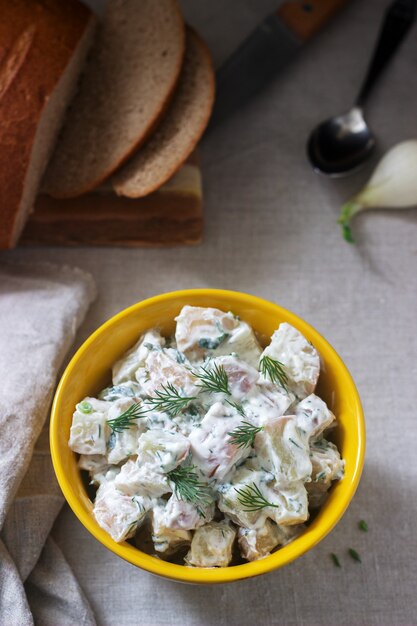 Salade de pommes de terre froide traditionnelle avec des oignons et des herbes sur un fond de nappe en lin. Style rustique.