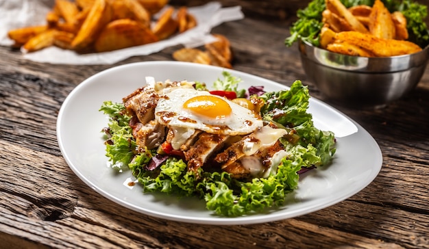 Salade de poulet avec œuf au plat et sauce sur une assiette blanche et bois rustique, avec des quartiers de pommes de terre sur un côté.