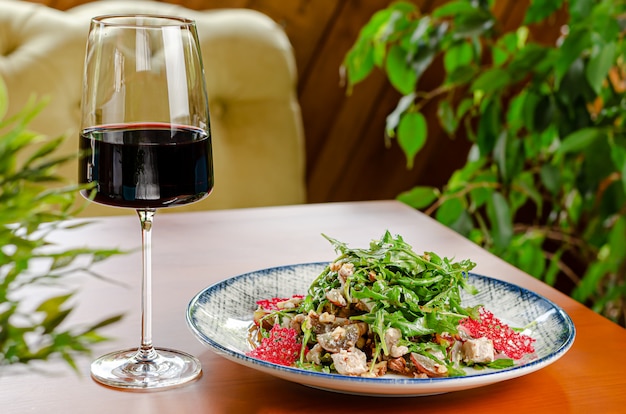 Salade de poulet à la roquette et vinaigrette aux noix servie avec un verre de vin rouge sur une table en bois. Copier l'espace