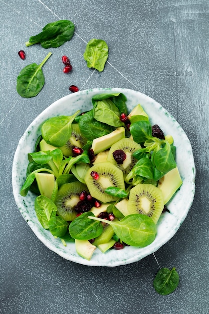 Salade de pousses d'épinards, cresson, kiwi, avocat et grenade dans une vieille assiette en céramique sur une surface de béton gris. Mise au point sélective. Vue de dessus. Copier l'espace