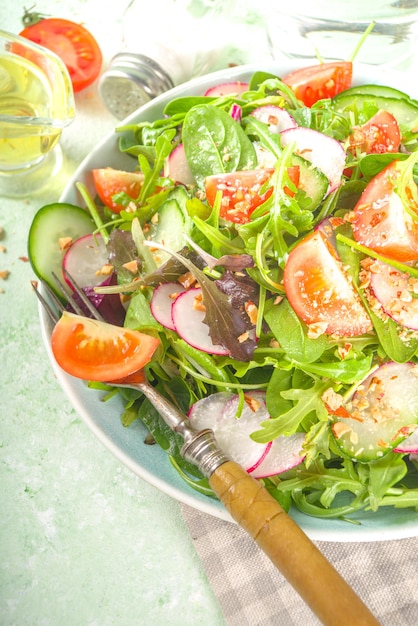 Salade printanière fraîche et colorée - avec tomates, avocat, noix, concombre, radis printanier, sur fond vert clair. Concept d'alimentation saine de régime de printemps