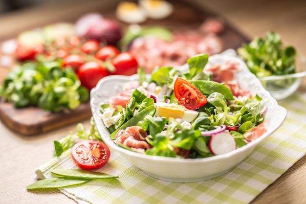 Salade printanière fraîche avec des feuilles vertes tomates oeuf radis oignon rouge jeunes pois prosciutto fromage feta et huile d'olive.