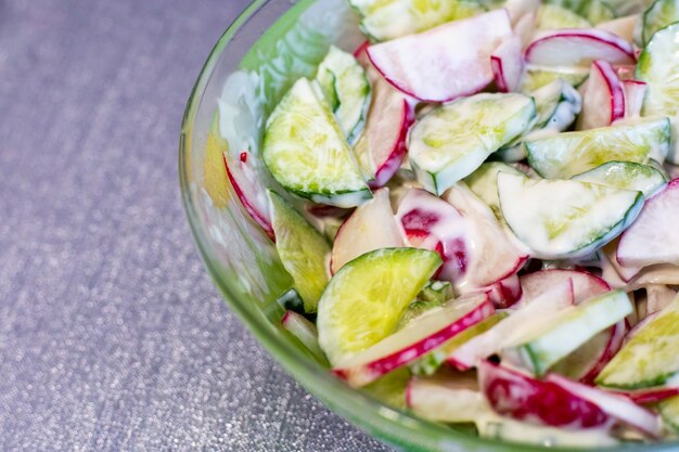 Salade printanière de radis et de concombre assaisonnée de sauce sur une assiette et fond texturé gris