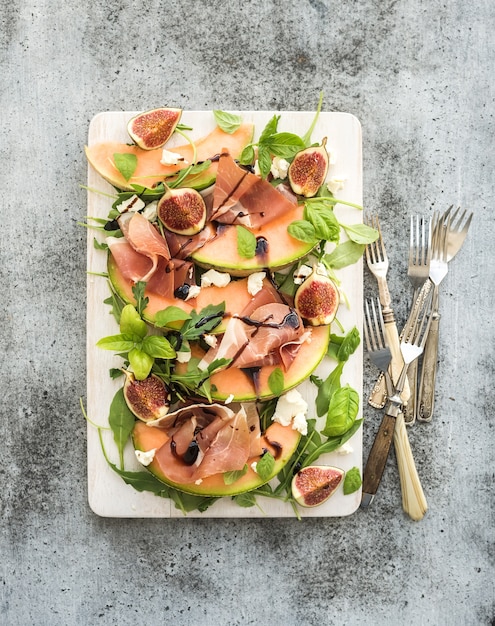 Salade de prosciutto, melon, figues et fromage à pâte molle sur un plateau blanc au-dessus de grunge