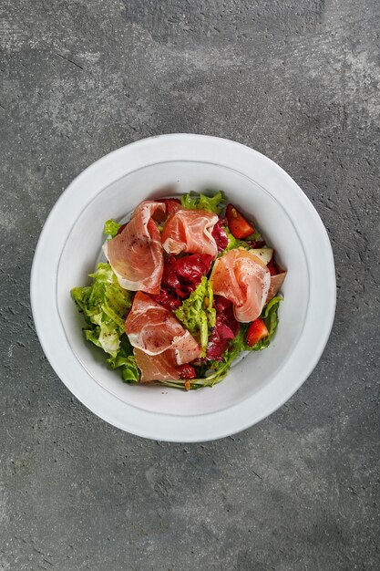 Salade de prosciutto en plaque blanche sur fond de béton gris