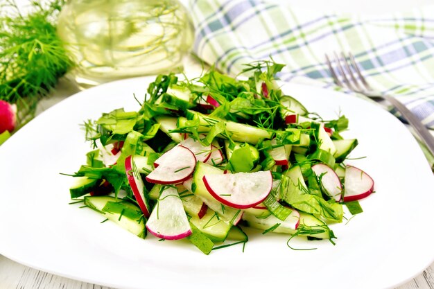 Salade de radis, concombre, oseille et légumes verts, habillée d'huile végétale dans une assiette sur fond de planche de bois