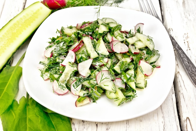 Salade de radis, concombre, oseille et légumes verts, habillée de mayonnaise dans une assiette sur fond de planche de bois clair