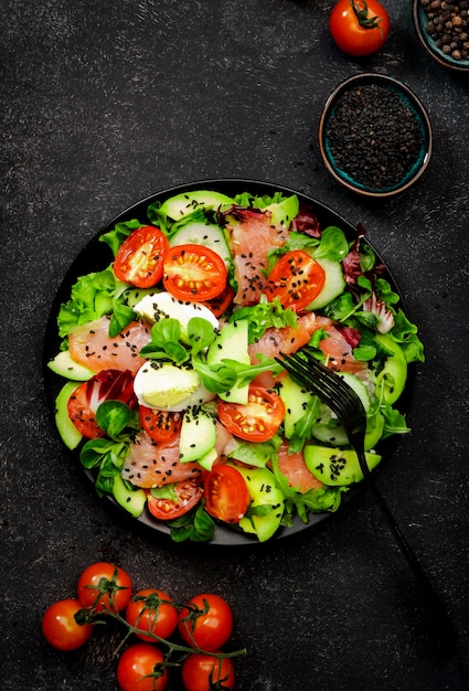 Salade de régime Keto avec saumon salé avocat oeuf graines de sésame huile d'olive tomates et herbes mélangées fond noir vue de dessus espace de copie