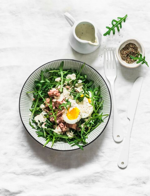 Salade de roquette au thon en conserve œuf à la coque et vinaigrette à la moutarde au yogourt sur fond clair vue de dessus