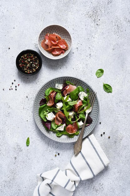 Salade de roquette, bettes au fromage bleu et prosciutto avec sauce sur fond de béton, vue de dessus.