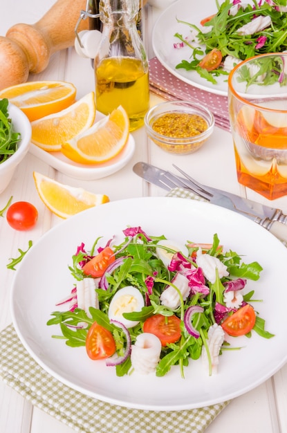 Salade de roquette, calmar, tomates cerises, oignons et oeufs de caille sur fond en bois blanc.