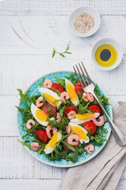 Salade de roquette, concombre, tomate, œufs et crevettes avec sauce soja sur plaque en céramique. Mise au point sélective. Vue de dessus.