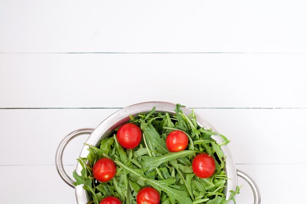 Salade de roquette fraîche aux tomates cerises dans un bol sur un fond en bois blanc. vue de dessus