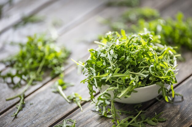 Salade de roquette fraîche dans un plat blanc sur une table en bois.