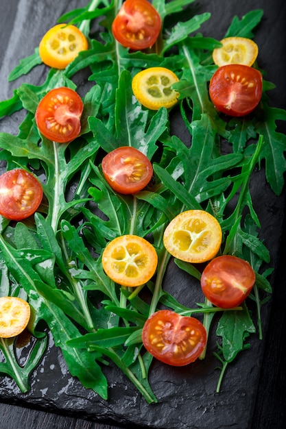 Photo salade de roquette fraîche avec kumquat et cerise de tomate sur plaque d'ardoise. vue de dessus. nourriture saine. régime.