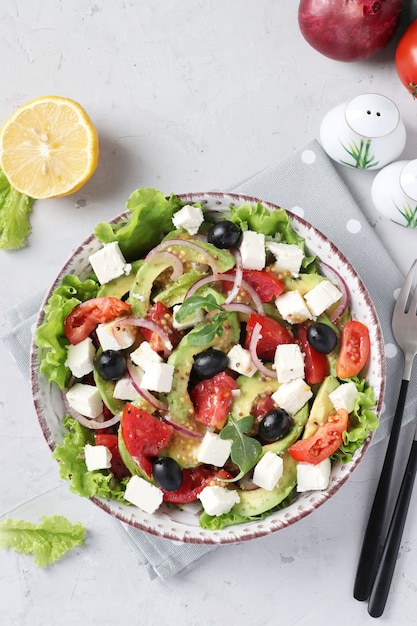 Salade saine avec avocat, tomates, feta, olives noires et oignon rouge sur fond gris