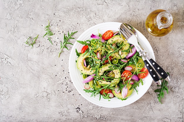 Salade saine de légumes frais - tomates, avocat, roquette, radis et graines sur un bol. Nourriture végétalienne. Mise à plat. Vue de dessus