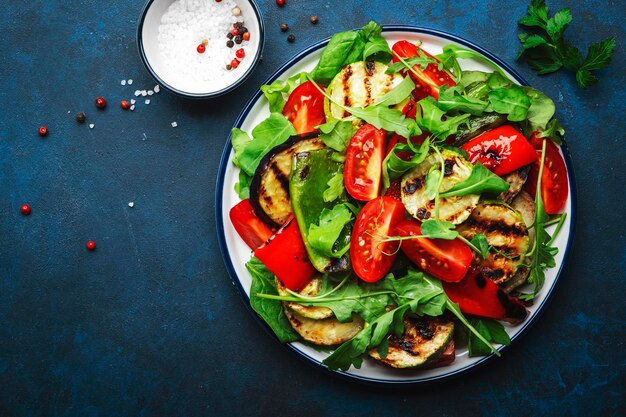 Salade saine avec légumes grillés paprika courgettes aubergines avec tomates fraîches et herbes mélangées fond de table bleu vue de dessus