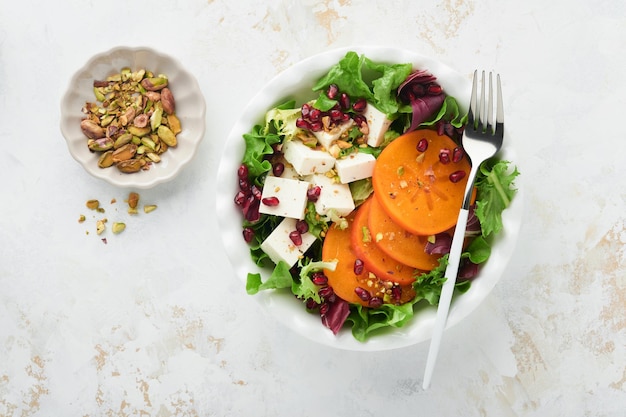 Salade Salade verte fraîche avec fromage feta, kaki, grenade et pistache sur une assiette blanche Idée pour une délicieuse salade de Noël d'hiver saine Alimentation saine et équilibrée Vue de dessus