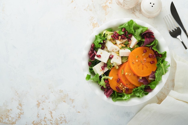 Salade Salade verte fraîche avec fromage feta, kaki, grenade et pistache sur une assiette blanche Idée pour une délicieuse salade de Noël d'hiver saine Alimentation saine et équilibrée Vue de dessus