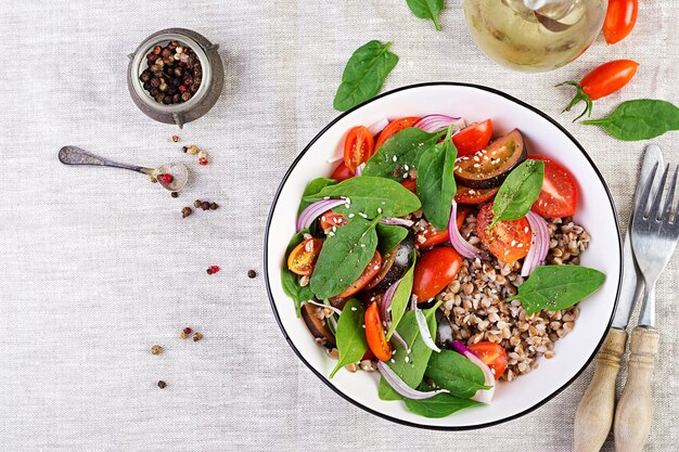 Salade de sarrasin avec des tomates cerises, oignon rouge et épinards frais. Menu végétalien.