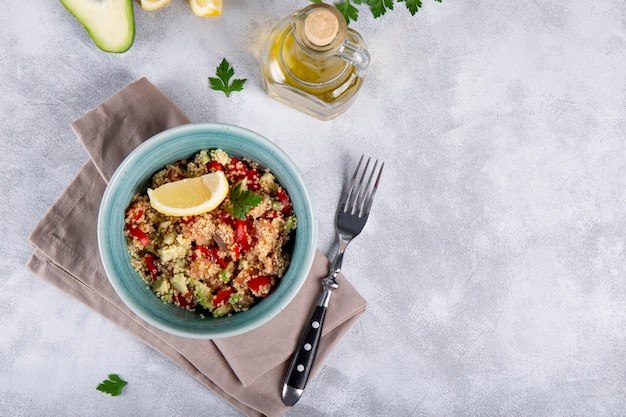 Salade de saumon aux tomates, avocat et quinoa dans un bol bleu sur une table gris clair voir un plat