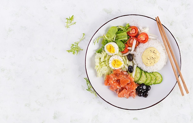 Salade de saumon biologique frais avec du riz, des œufs bouillis, des tomates, du concombre et des olives noires. Concept de nutrition rapide et sain pour le déjeuner. Vue de dessus à plat