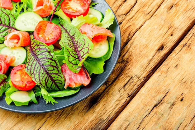 Salade de saumon salé, légumes et herbes en assiette sur une vieille table en bois.