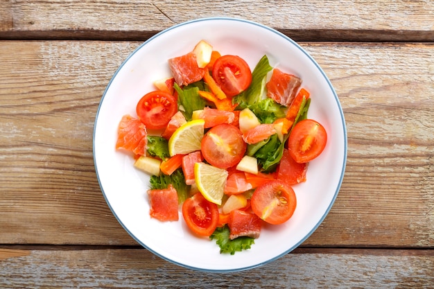 Salade de saumon et tomates cerises et salade verte dans une assiette sur une table en bois