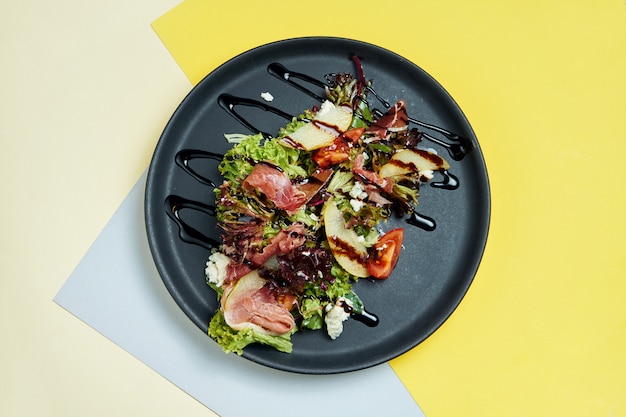 Salade savoureuse avec laitue, jambon serrano, poire, tomates cerises en plaque noire. Vue de dessus