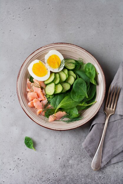 Salade scandinave au saumon rose fumé, épinards, concombre et œuf de poule dans un plat en céramique grise. Vue de dessus.