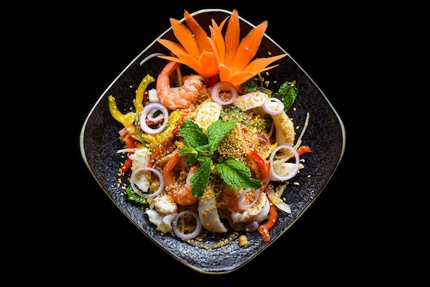 Salade thaïlandaise faite de crevettes et de calmars et d'oignons isolés sur la vue de dessus de fond noir